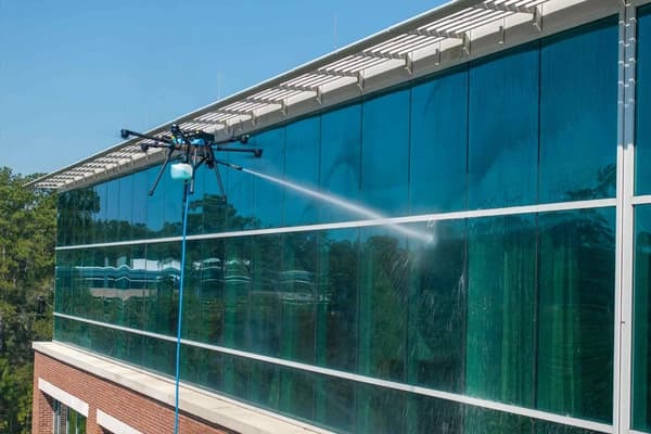 A drone pressure-washing the glass facade of a multi-story building.